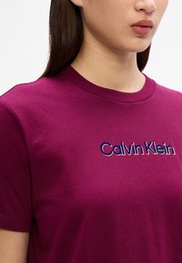 Fuchsia bomull T-skjorte med korte ermer og rund hals, med brodert "Calvin Klein" logo i blått og hvitt på framsiden.
