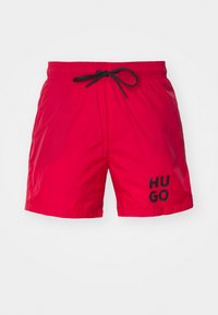 Shorts de bain rouges avec une taille élastique, cordon de serrage noir et logo "HUGO" noir sur la jambe gauche. Texture légère et lisse.