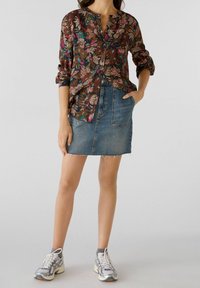 Femme portant un blouse à manches longues à fleurs, une mini-jupe en denim avec des poches avant, des chaussettes grises et des chaussures de course grises et blanches.