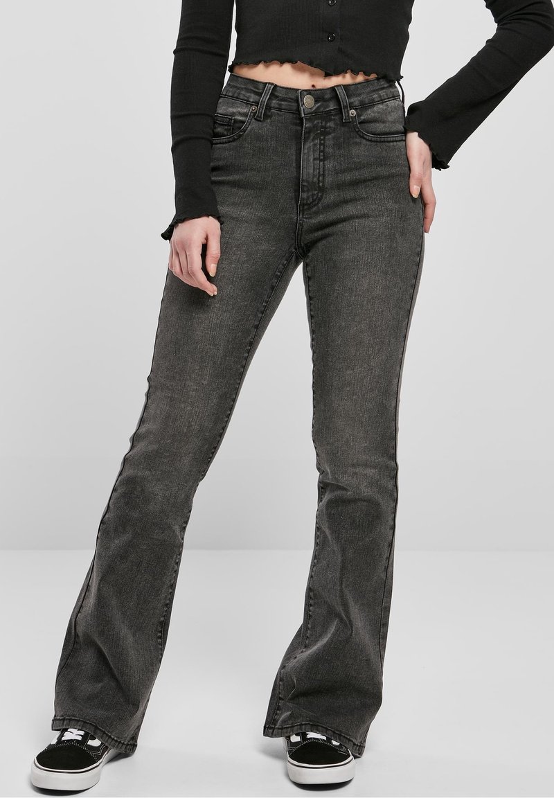 Jeans negros acampanados con textura desgastada, cintura media, cinco bolsillos y detalles sutiles en las costuras. Combinados con zapatillas negras y blancas.