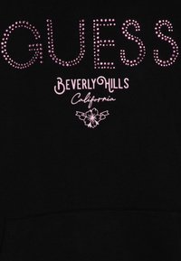 Czarna bluza z kapturem z napisem "GUESS" wysadzanym cyrkoniami, z poniżej nadrukiem "Beverly Hills" i "California" w różowym kolorze. Miękka tekstura, standardowy krój z kapturem.