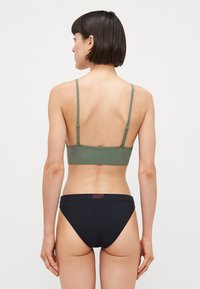 Olivovo zelený bralet s nastaviteľnými ramienkami v kombinácii s čiernymi bikínovými nohavičkami s logovými pásmi. Hladká tkanina, jednoduchý dizajn, minimalistický štýl.