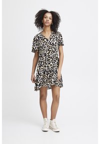 Leopardenmuster Shirtkleid mit V-Ausschnitt und kurzen Ärmeln, aus leichtem Stoff. Kombiniert mit weißen High-Top-Sneakern.