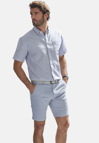 Kurzärmeliges, knöpfbares Hemd mit blau-weißen Streifen, kombiniert mit hellblauen Shorts. Verfügt über eine Brusttasche und einen Gürtel.