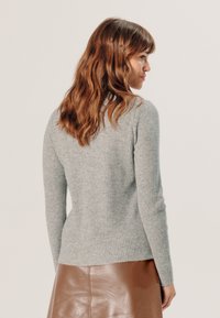 Grijze geribbelde trui met lange mouwen, aansluitende pasvorm en fijne textuur, gecombineerd met een bruine leren rok. Achteraanzicht weergegeven.