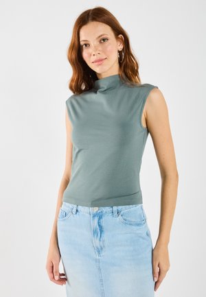 Figurbetontes, ärmelloses Turtleneck-Oberteil aus einem gedämpften grünen Stoff, kombiniert mit einem hellblauen Jeansrock mit einem Schlitz vorne und klassischen Knopfdetails.