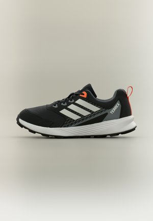 Černobílá běžecká bota Adidas Terrex s oranžovými akcenty, silnou podrážkou a třemi bílými bočními proužky, zobrazená z pravé strany.