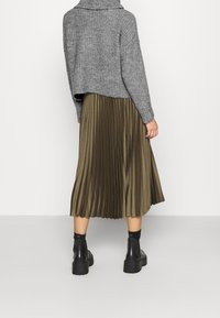 Grau gestrickter, kurzer Pullover, olivgrüner plissierter Midirock und schwarze Stiefeletten mit klobiger Sohle, Blick von hinten.