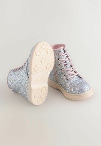 Botines brillantes plateados con acentos rosa, puntera redonda, cordones frontales y suela de goma texturizada con patrones de estrellas.