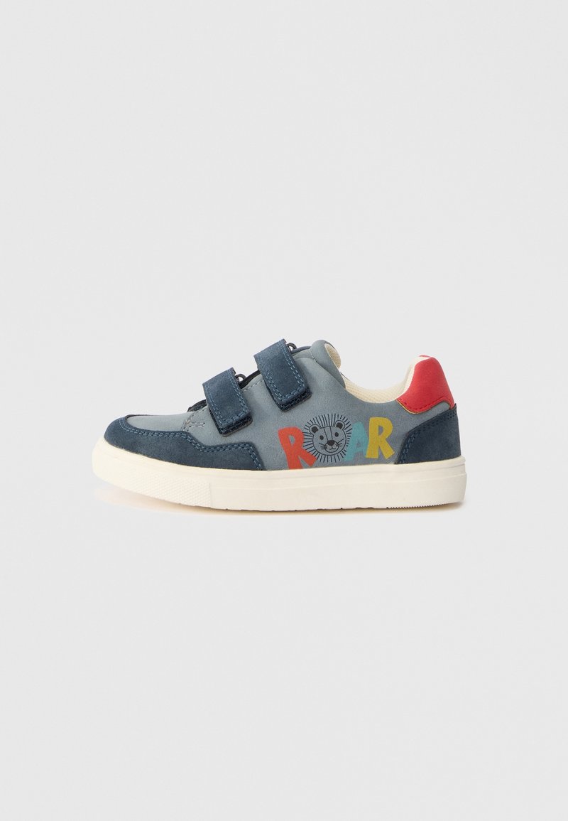 Baskets enfant bleu et gris avec deux bandes Velcro, languette rouge au talon et texte multicolore "ROAR" avec un dessin de lion sur le côté.