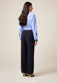 Hellblaues Langarmhemd mit knöpfbaren Manschetten, kombiniert mit hoch taillierten, weit geschnittenen, navyblauen Hosen und schwarzen, hochhackigen Sandalen, von hinten gesehen.