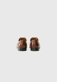 Zapatos de cuero marrón con una textura lisa, diseño de punta redonda, tacón bajo negro y detalles bordados en la parte trasera. Vista trasera mostrada.