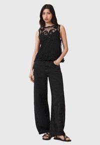 Čierny bezrukávový top s kvetinovou čipkovou vrstvou a oblým výstrihom; v kombinácii so širokými čiernymi nohavicami. Modelka má na nohách čierne sandále.