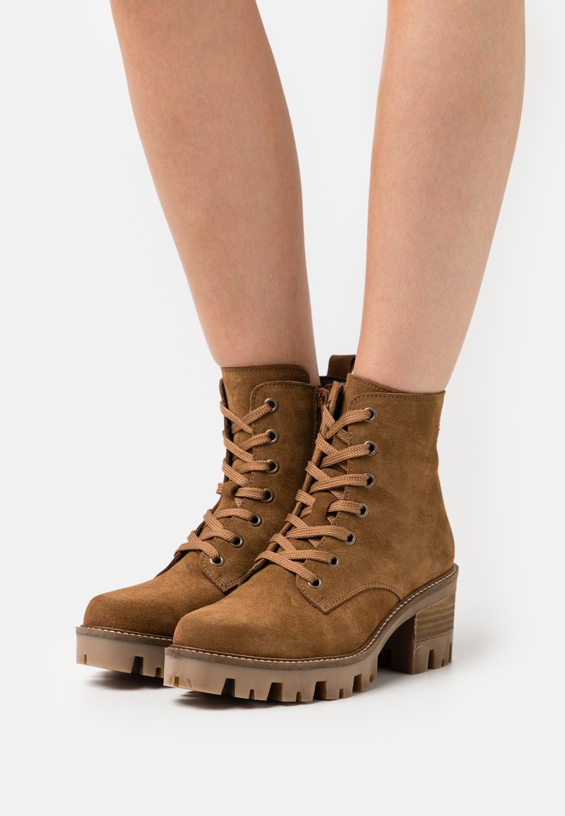 Botas de tobillo de ante marrón con acabado texturizado, puntera redonda, parte delantera con cordones y tacón grueso y estriado, que cuenta con ojales de metal y una cremallera lateral.