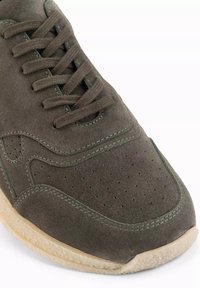 Sneaker in suede verde scuro con tomaia perforata, punta tonda e design con lacci piatti. Suola color crema con superficie texturizzata.