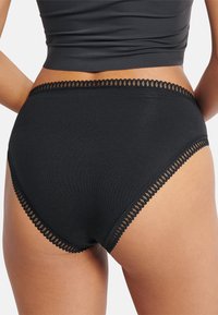 Zwarte katoenen hoge taille slipjes met een geschulpte kantafwerking langs de tailleband en beenopeningen. Gladde textuur en volledige bedekking.