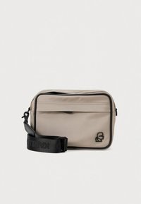 Piccola borsa rettangolare in tessuto beige chiaro con due scomparti con cerniera. Presenta una tracolla regolabile nera con logo e un dettaglio con logo cucito.