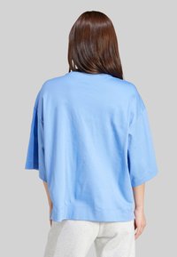 Svetlomodré nadmerné tričko s krátkymi rukávmi, vyrobené z mäkkej bavlnenej tkaniny, s rovnou spodnou časťou a minimálnymi detailmi šitia.