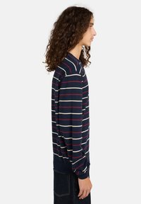 Maglione blu navy con strisce orizzontali rosse e crema. Maniche lunghe, collo a giro, e polsini a coste. Texture liscia, vestibilità casual.