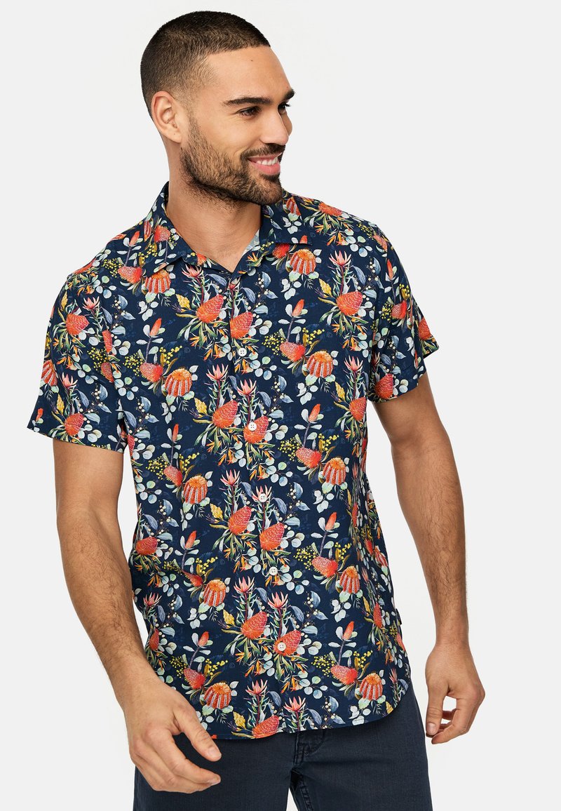 Camisa de manga corta con un fondo azul marino oscuro y vibrantes patrones florales en rojo, verde y blanco. Hecha de un tejido ligero.