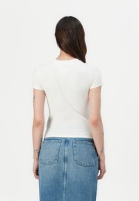 Vit kortärmad t-shirt med en figurnära design, tillverkad av ett smidigt, elastiskt tyg, kombinerad med en högmidjad jeanskjol.