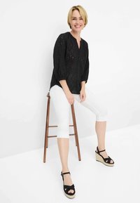 Blusa nera texturizzata con scollatura a V e maniche 3/4, abbinata a pantaloni bianchi a tre quarti e sandali neri con zeppa e suola intrecciata.