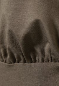 Brun stoffoverdel med samlet tekstur i midjen, med en glatt, elastisk finish og subtil ribbing gjennom hele.