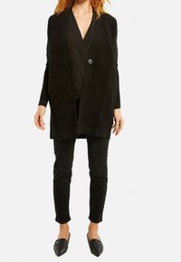 Černý žebrovaný kardigan s jedním stříbrným knoflíkem, přes černý top. V kombinaci s černými slim kalhotami a plochými černými botami.