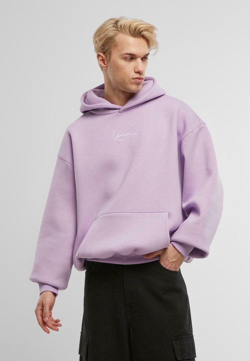 Felpa oversize lavanda realizzata in tessuto morbido, con tasca frontale e ricamo del logo bianco. Il modello la indossa con una gonna scura.