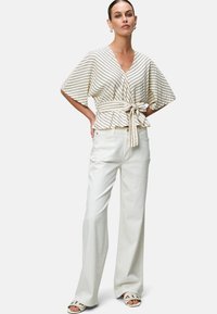 Striped cream wrap top with kimono sleeves, tied at the waist. Paired with wide-leg white trousers and light-colored sandals.