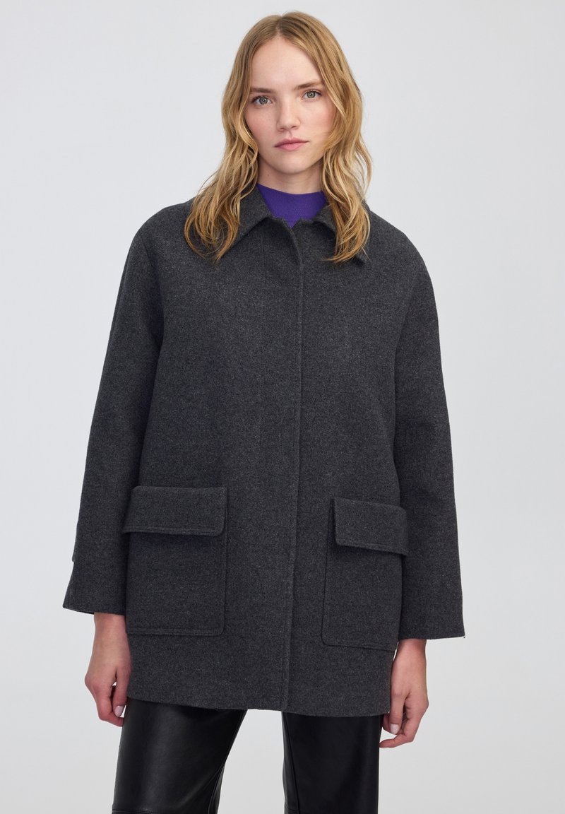 Cappotto grigio in lana con colletto, tasche laterali e taglio dritto. Presenta una finitura testurizzata e un design fino al ginocchio.