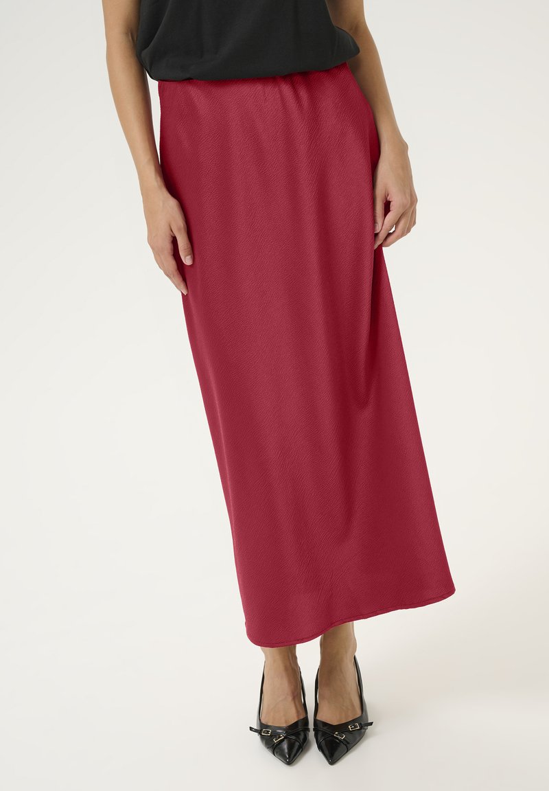 Longue jupe rouge fluide en tissu lisse, dotée d'une taille élastique. Associée à des escarpins noirs à bout pointu pour le contraste.