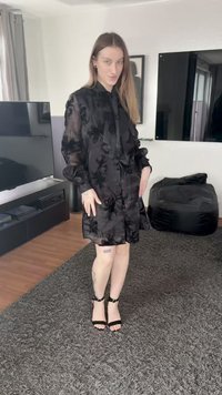 Black, sheer dress with floral patterns, button closure, and long sleeves. Worn with black strappy sandals on a textured carpet.