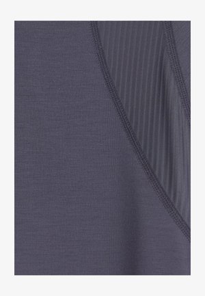 Close-up van donkergrijs stof met gladde en geribbelde textuursecties gescheiden door zichtbare dubbelgestikte naden.