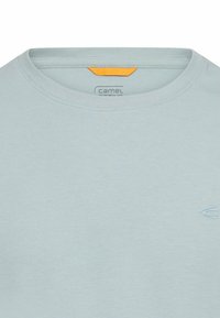 Jasnoniebieski bawełniany t-shirt z okrągłym dekoltem, z małym logo w dopasowanym odcieniu oraz pomarańczową metką z tyłu.