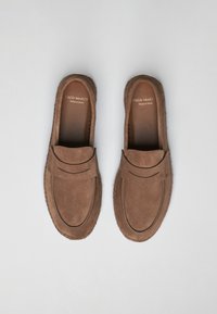 Brune suede loafers med rund tå og et syet accentbånd foran. Lavet i Spanien, med en struktureret ydersål.
