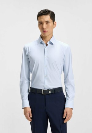 Lichtblauwe button-up overhemd met kleine witte stippen, lange mouwen en een puntkraag, gecombineerd met donkere broeken en een zwarte riem.