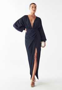 Námorníckomodrá dlhá šaty z hladkého materiálu, s hlbokým V výstrihom, vzdušnými rukávmi, bočným rozparkem a zberanými detailami v páse.