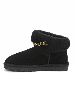 Botas de tobillo de ante negro con un puño de piel negra esponjosa y detalle de cadena dorada. Suela plana de goma negra y diseño cosido a lo largo de los lados.