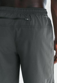 Szare szorty sportowe z elastycznym paskiem w talii, z zamykaną na zamek tylną kieszenią i gładką teksturą materiału. Minimalistyczny biały detal z logo.