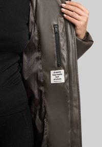Jacket roz din material moale cu exterior neted și un buzunar cu fermoar. Interiorul prezintă o etichetă cu textul: "O îmbrățișare călduroasă din țesătură."