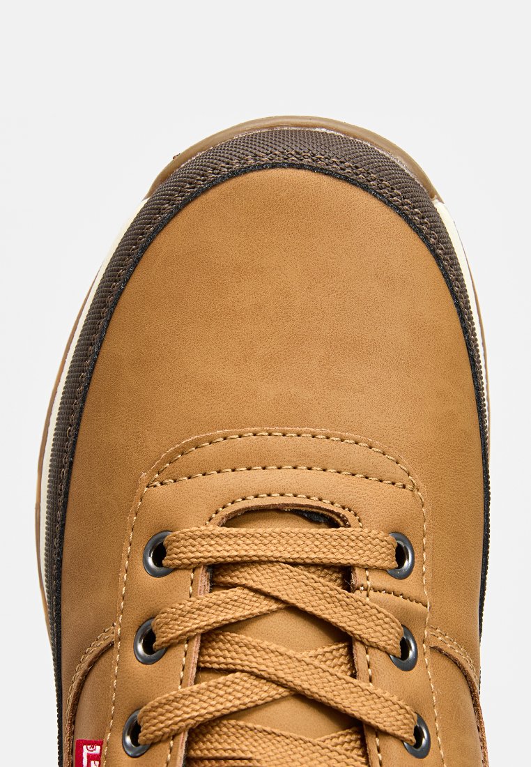 Sneaker in pelle marrone con texture liscia, punta tonda, lacci nocciola e dettagli neri. Presenta un colletto imbottito e decorazioni a motivo sulla punta.