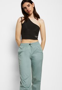 Top cropped preto de um ombro, tecido texturizado; combinado com calças verde claro de cintura elástica, com cordão e bolsos laterais.
