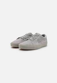 Helle graue Wildleder-Sneaker mit einem Niedrigschuh-Design, auffälligen Schnürsenkeln, Perforationen an der Vorderseite und einer strukturierten Gummisohle.