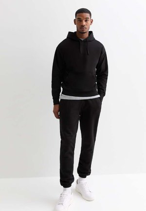 Hoodie noir avec cordon de serrage, associé à un jogging noir assorti. Design épuré, tissu doux et baskets blanches sportives.