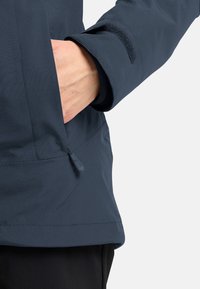 Giacca impermeabile blu navy con una texture liscia, tasca con zip e chiusura a velcro sui polsini per un fit regolabile.