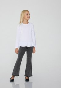 Bílá košile s dlouhými rukávy a volánkovým lemem, spárovaná s rozšířenými černými džíny. Černé baleríny doplňují outfit. Jednoduchý a moderní design.