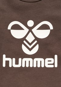 Bruine stof met een witte afbeelding van een gestileerd logo in de vorm van een bij en het woord "hummel" in vetgedrukte, afgeronde letters.