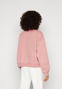 Sudadera rosa con un corte relajado, hombros caídos y dobladillo acanalado. Fabricada con material suave, presenta mangas largas y un diseño minimalista.