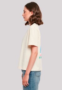 Cremefarbiges T-Shirt aus Baumwolle mit kurzen Ärmeln und buntem Grafikdesign auf der Rückseite. Gerader Schnitt mit sichtbaren Nähten und lässiger Passform, kombiniert mit Jeans.